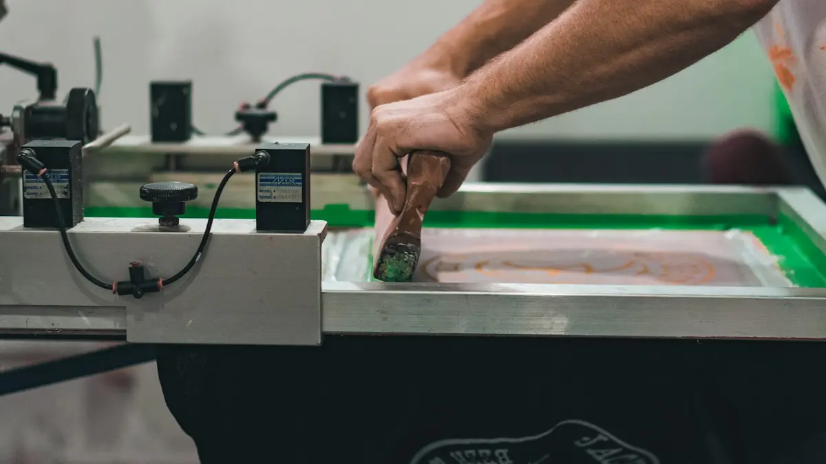 A person screen printing on a textile using a squeegee and printing frame.