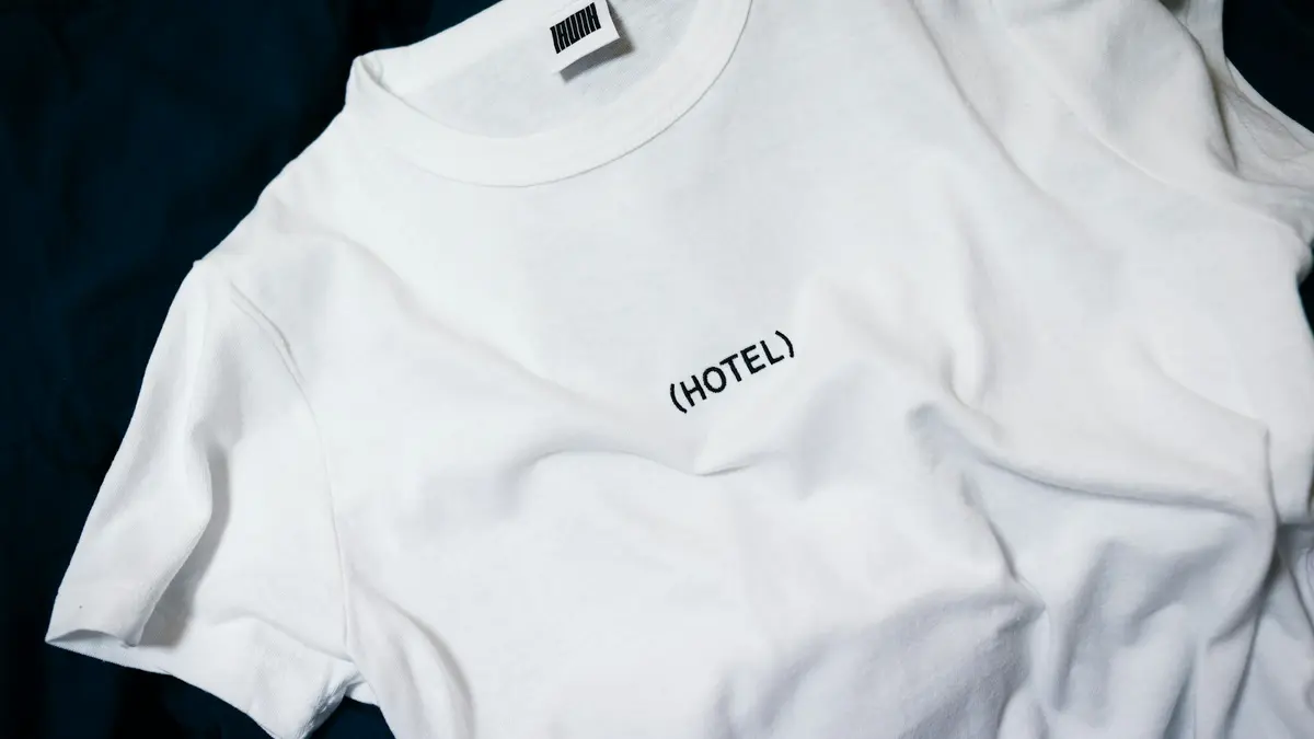 White t-shirt featuring the word &ldquo;(HOTEL)&rdquo; printed in black.